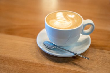 Kafedeki ahşap masanın üzerinde duran sütlü kahve tabağı. Süt süslemeli kapuçino. Sabah kahvaltısı