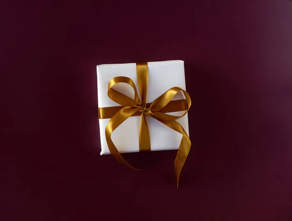 Caja de regalo envuelta en papel blanco con un lazo dorado sobre fondo violeta festivo —  Fotos de Stock