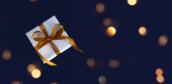 Banner of Gift box wrapped in white paper with a golden bow on festive violet background — стоковое фото