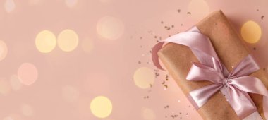 Banner of Birthday or New Year present in kraft paper with pink ribbon on soft beige background with glitter