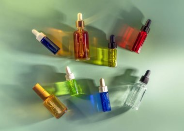 Transparent glass dropper bottles with green, red and blue liquid inside on mint emerald background in the sunlight
