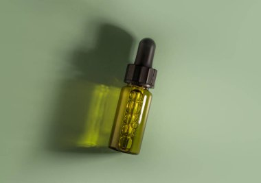 Güneş ışığının zümrüt zümrüt zemininde yeşil sıvı bulunan şeffaf cam damlası şişesi.