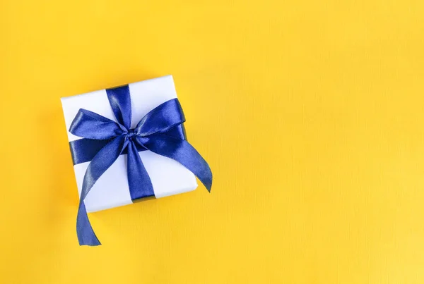 Bannière d'un cadeau enveloppé dans du papier blanc avec un arc bleu en satin sur fond orange jaune festive — Photo