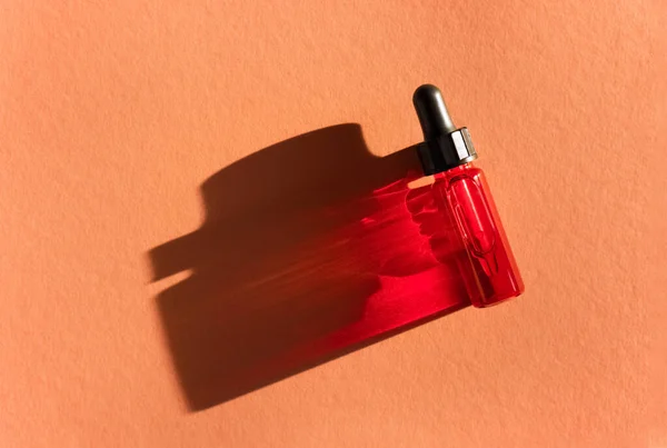 太陽光の下でベージュ色の背景に赤い液体と透明なガラスのドロッパーボトル 流体ヒアルロン酸とピペット レチノール 化粧品 美しさ — ストック写真