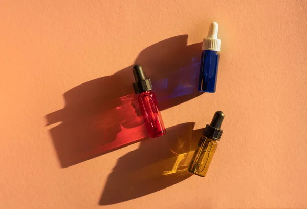 Průhledné skleněné kapátko lahvičky se žlutou, zelenou, červenou a modrou tekutinou uvnitř na béžovém pozadí ve slunečním světle — Stock fotografie