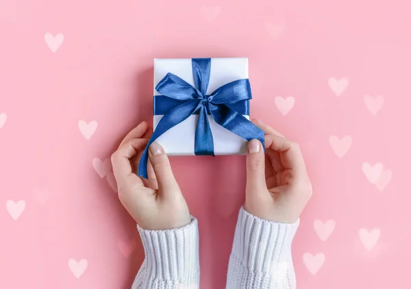 Female Hands holding a gift in white wrapping paper on pink background — Stock Photo, Image
