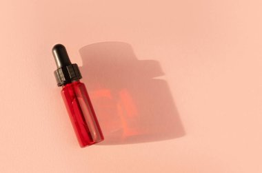 Şeffaf cam damlatan şişelerin içinde kırmızı sıvı bej arka planda güneş ışığı