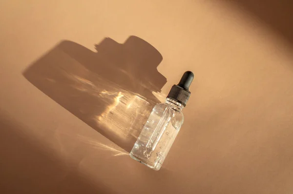 Průhledná skleněná kapátko láhev se vzduchovými bublinkami na béžovém pozadí ve slunečním světle — Stock fotografie