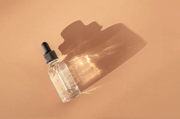 Flacon compte-gouttes en verre transparent avec bulles d'air sur fond beige à la lumière du soleil — Photo