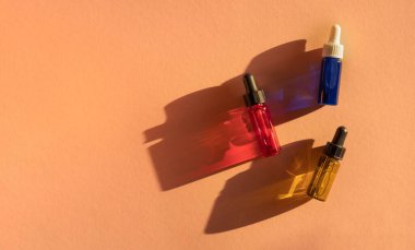 İçinde yeşil, kırmızı ve mavi sıvı bulunan şeffaf cam damlaları güneş ışığında bej arka planda. Pankart