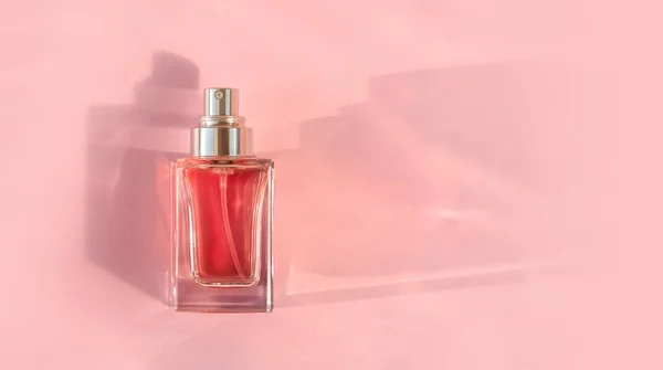 Baner przezroczystej butelki perfum leżącej na różowym tle — Zdjęcie stockowe