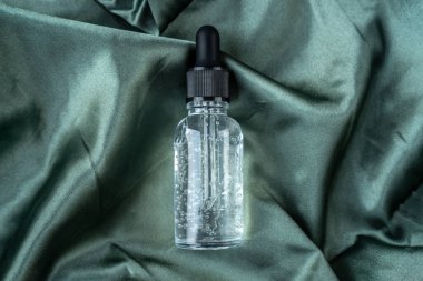 Cam kozmetik şişesi, pürüzsüz mavi ipek ya da saten katlar. Kumaş dokusu arka planı. Soyut duvar kağıdı