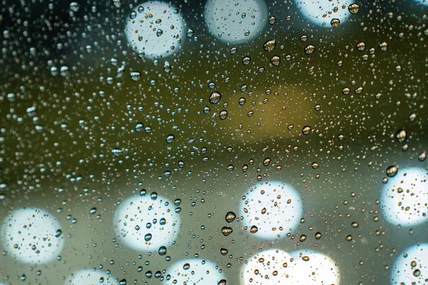 Pencere camına yağmur damlaları ve arka planda ışık. Yumuşak odak