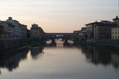 Gün batımında bir nehrin aşağısına bakın. Her iki tarafında binalar ve uzaklarda kano olan biri.