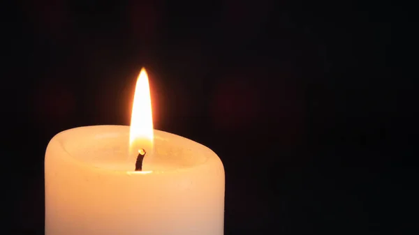 burning white candle close up on black background