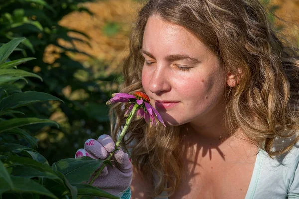 Evdeki sebze bahçesinde Echinacea çiçeği koklayan genç bir kadın.