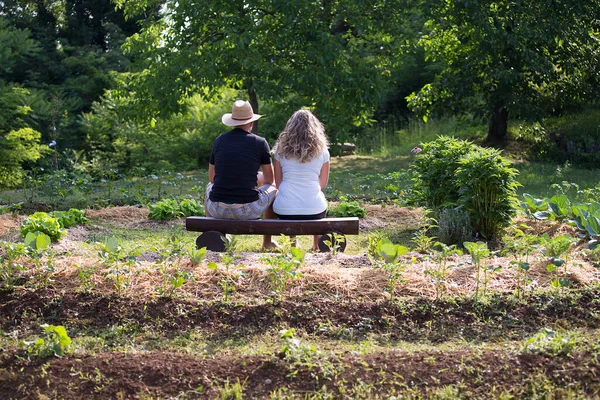 Genç bir adam ve kadın evde yetişen sebze bahçesinde oturup sohbet ediyorlar.
