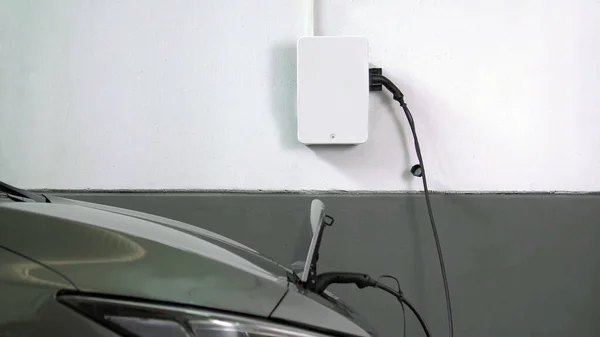 Close-up of a home electric charging station charging a gray electric car