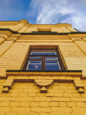 Pencerenin altında Yahudi menorası şeklinde dekorasyonu olan eski bir evin sarı tuğlalı duvarı, aşağıdan görünüyor. Eski bir tuğla evin penceresindeki Ortodoks Hıristiyan kilisesinin tepesindeki haçın yansıması.. 