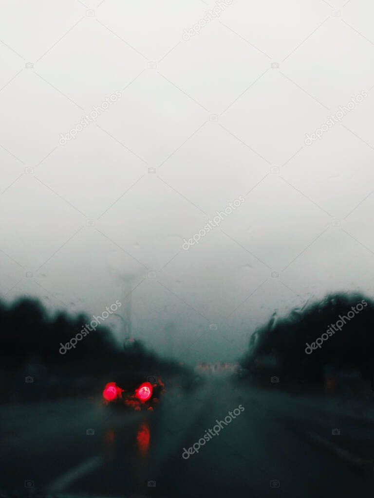 a car with defocused headlights in the rain is visible through the car's windshield