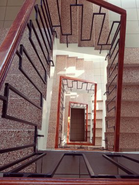 Çok katlı bir binanın merdiven boşluğunun üst görüntüsü dikdörtgen spiral bir merdiven ve tırabzanlar benzersiz bir geometrik desen oluşturuyor.