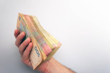 Human hand holds a stack of Ukrainian hryvnia banknotes on a light background. Money and finance concept. Financial background. Money of Ukraine. 