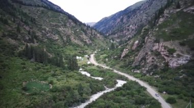 Bir araba, yeşil ormanı, vahşi nehri ve yurdu geçen bir helikopter tarafından takip ediliyor.