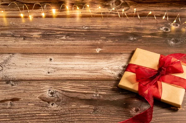 Ahşap arka planda bir hediye. Hediye kağıdına doldurulmuş Noel ışıkları süslemesi.