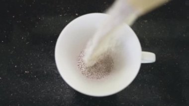 Siyah bir masanın üzerindeki beyaz bardağın en üst görüntüsü. Sütlü hazır kahvenin döküldüğü yer. Sabahları poşetlerden hızlı demlenmiş kahve yapmak için güzel bir çekim. 4K.