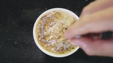 Siyah bir masanın üzerinde duran beyaz bir bardakta demir kaşıkla çabucak demlenen bir adamın üst görüntüsü. Sabah kahvesini köpük ve köpükle karıştıran bir adamın yakın çekimi. Yakın plan.