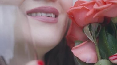 Yüzünün yanında bir buket kırmızı gül ve şeffaf bir bardak tutan bir kızın gülümsemesi. Hayatında önemli bir törende yanağında gözyaşı olan duygusal bir kadının gülümsemesi.
