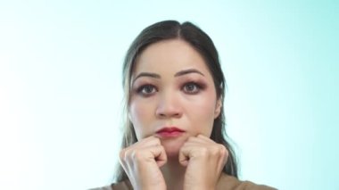 Uzun saçlı güzel bir kız açık yeşil arka planda yumruklarıyla yaşlanmayı önleyen bir yüz masajı yapıyor. Kırmızı manikürlü Asyalı bir kadın ağır çekimde yüz masajı yapıyor. Kapat..