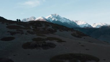 Karanlık tarlaların üzerinde uçuşan destansı bir manzara. Arkasında yeşil çalılar ve karla kaplı büyük kayalık dağlar var. Resimli, sinematik bir dron vadide uçuyor.