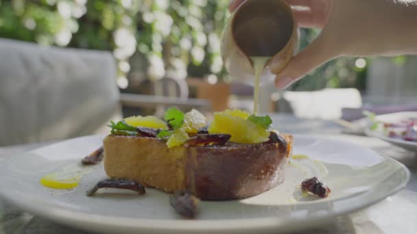 Primer plano de un exquisito brindis francés con rodajas de naranja en un plato blanco. Un hombre vierte leche condensada en tostadas francesas en un restaurante luminoso. Delicioso postre con bollo y dulce en cámara lenta — Vídeos de Stock