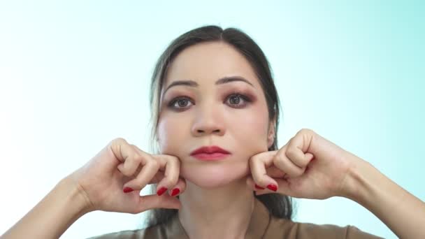 Una hermosa chica con el pelo largo hace un masaje facial antienvejecimiento con los puños sobre un fondo verde claro. Una mujer asiática con una manicura roja hace un masaje facial en cámara lenta. De cerca.. — Vídeos de Stock