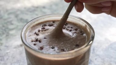Yakın plan. Pembe manikürlü bir kız eli hafif mermer bir tezgahın üzerinde kamışla çikolata parçacıklı bir kakao kokteyli karıştırıyor. Ferahlatıcı, nefis bir smoothie içeceğinin yakın çekimi. güneşli bir gün.