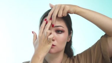 Uzun saçlı güzel bir kız yeşil bir arka planda parmaklarını yüzünün derisine bastırarak yüz masajı yapıyor. Kırmızı manikürlü Asyalı bir kadın yüz masajı yapıyor..