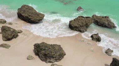 Plajın üst manzarası beyaz kum ve zümrüt yeşili dalgaların kırıldığı büyük kırmızı kayalarla paylaşılır. Güneşli bir günde Balis Paradise plajı. Tropik bir adanın kıyı şeridi. 4k ağır çekim