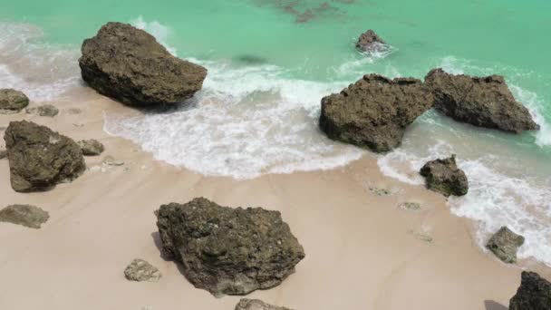ビーチのトップビューは、エメラルドグリーンの波が壊れ白い砂と大きな赤い岩と共有します。晴れた日にはバリスパラダイスビーチ。熱帯の島の海岸線。4kスローモーション — ストック動画