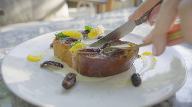 Beyaz tabakta portakal dilimleri olan nefis bir Fransız tostunun yakın çekimi. Parlak bir restoranda bir parça Fransız tostunu bıçakla kesen adam. Tatlı tatlı, çörek ve ağır çekimde tatlı..