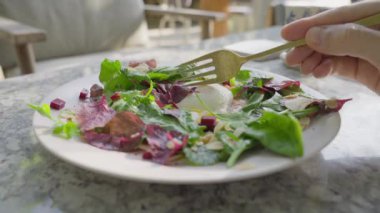 Güneşli bir günde, kişi parlak bir restoranda kahvaltı yapar ve haşlanmış yumurtayı çatalla keser. Adam çatalla yumurta keser ve bir parça alır. Mermer bir masada duran beyaz bir salata tabağının yakın çekimi.