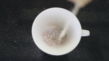 Siyah bir masanın üzerindeki beyaz bardağın en üst görüntüsü. Sütlü hazır kahvenin döküldüğü yer. Sabahları poşetlerden hızlı demlenmiş kahve yapmak için güzel bir çekim. 4K.