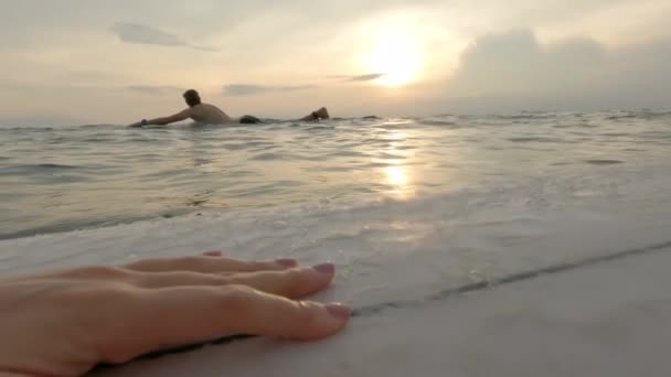 Pov af surfer pige med smuk lyserød manicure ser på surfer svømning i havet på baggrund af en solnedgang på en varm sommerdag. Et par surfere svømmer i havet og venter på bølger. Langsom bevægelse. – Stock-video