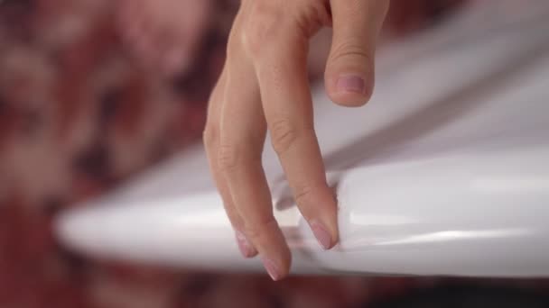 Een man met een slordige roze manicure raakt een witte surfplank aan geslagen door een klap. Close-up van een meisje dat een scheur op een surfplank aanraakt, na schade. Een persoon bereidt een surfplank voor reparatie. Langzame beweging. — Stockvideo