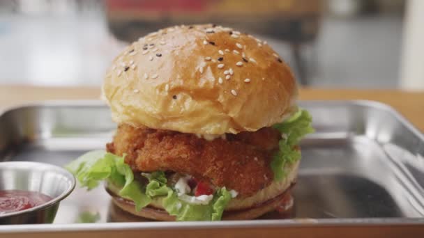 Dolly shot. A close-up of an appetizing juicy burger on a steel tray with red tomato ketchup in a sunny cafe. A large hamburger stands on a wooden table in an open-air restaurant. slow motion. — Stock Video