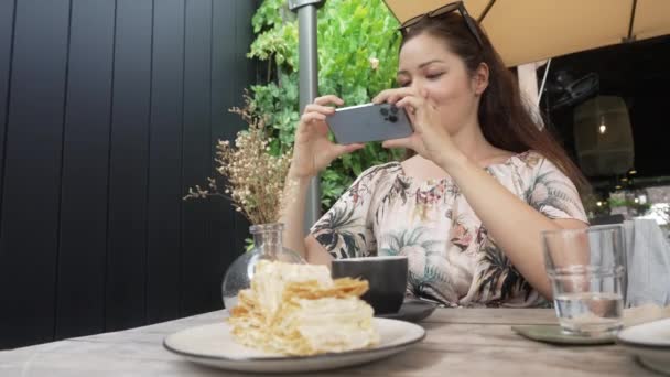 Bali, Indonesia - Nov 26, 2021: A beautiful Asian blogger takes pictures of food in a cafe on the new apple iphone 13 pro. Traveler girl in Bali takes pictures on her phone of a table. Slow motion. — Stockvideo