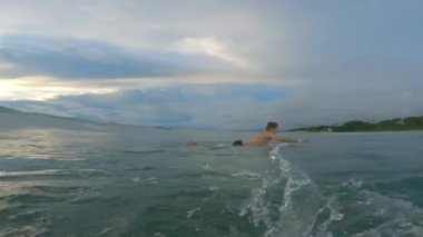 Dalgayla başlayan ve hemen yanındaki sörfçüye bakan bir sörfçü. Dalgaların arasından hızla ayrılıyor. Güneşli bir yaz gününde aynı dalgada birlikte sörf yapmak eğlenceliydi. Şortlu sörfçü dalga sürüyor.