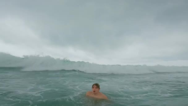 Un joven surfista en el océano se aferra a una tabla y se sumerge bajo una gran ola fuerte, agita con su fuerza arranca la tabla de surf de sus manos, la lanza al aire y se retuerce. Momentos peligrosos en el océano. — Vídeos de Stock