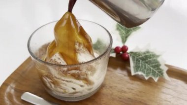 Yılbaşı kahvesi, affogato. Yukardan kahve dökülen karlı dağ şeklinde şeffaf camlı dondurma harika bir içecek oluşturur. Arka planda kırmızı böğürtlenli Noel kutlaması var.