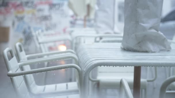 Mesas blancas y sillas de un restaurante callejero bajo la lluvia sobre el fondo de una pared con graffiti de colores. Mesas vacías y sillas de un café cerrado sobre el fondo de una calle con coches de paso — Vídeos de Stock